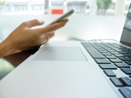 A smartphone is being used near an open laptop.