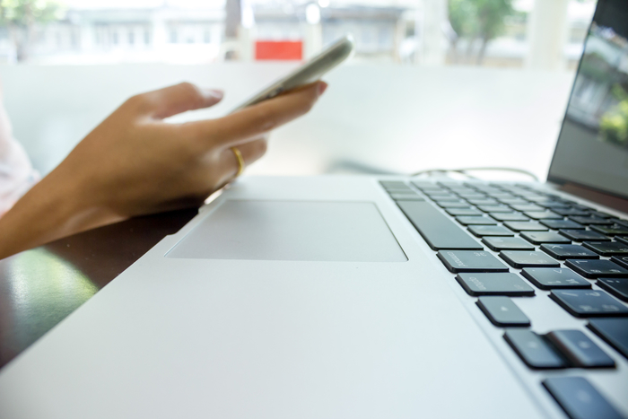 A smartphone is being used near an open laptop.