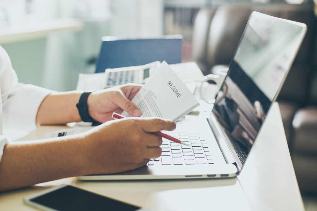 Man holding CV in front of laptop